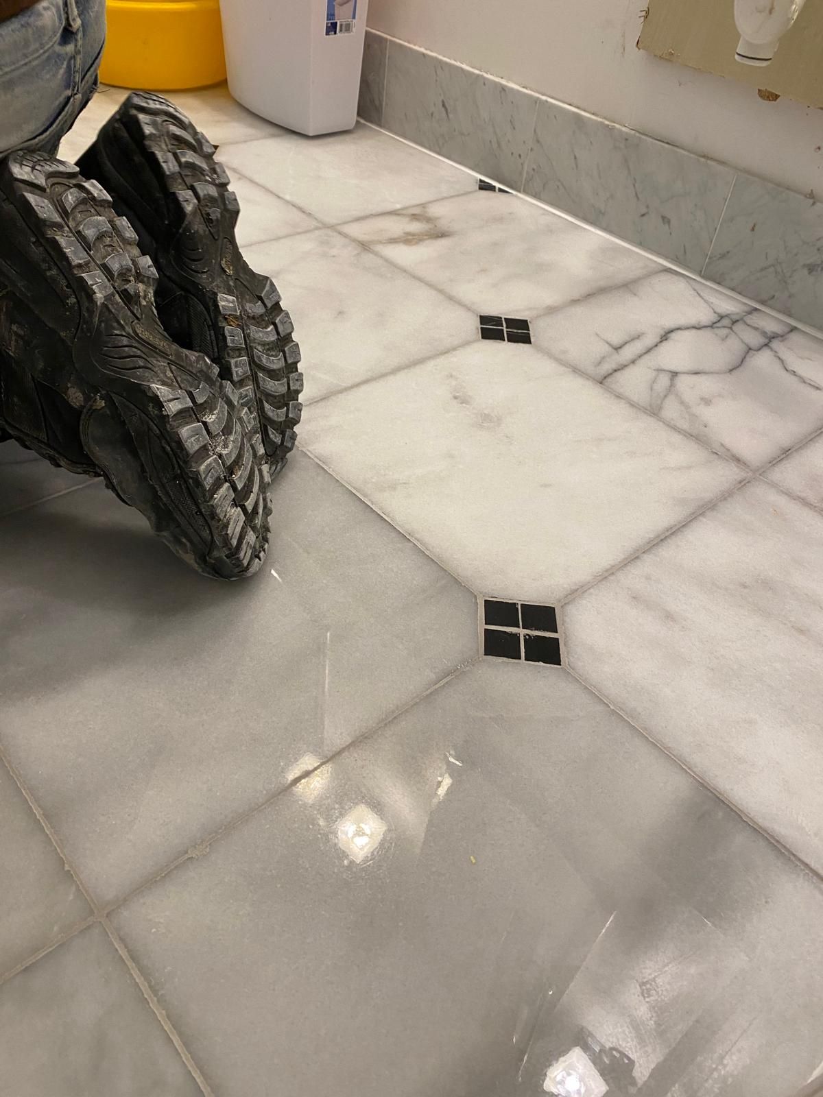 Person's boots on a white marble tile floor with dark accent squares.