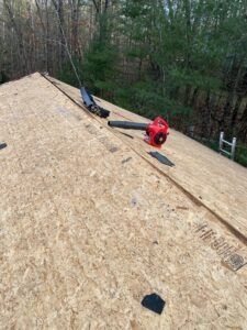 OSB roof with a red blower; trees in the background.