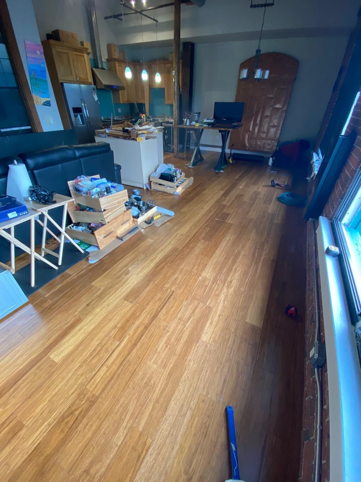 Wooden floor in a living space with a kitchen visible in the background, a TARDIS prop, and clutter.