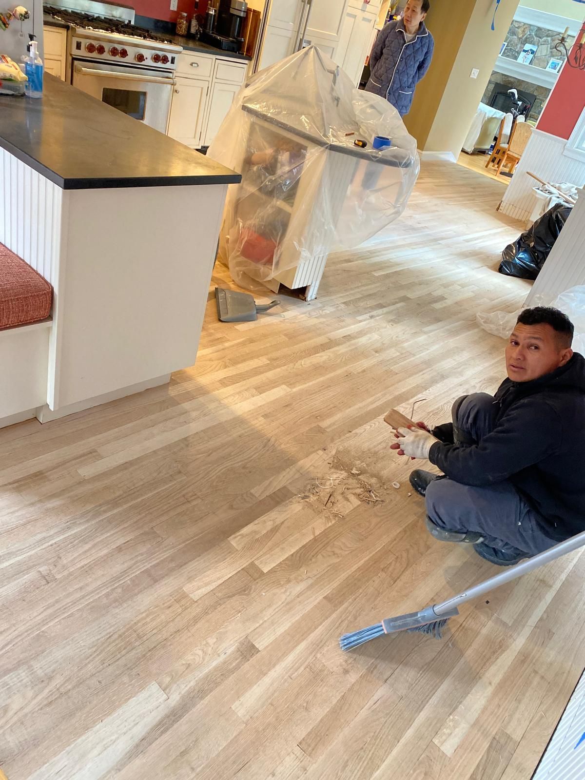Man cleaning hardwood floor in a kitchen. Another person and dust containment system in the background.