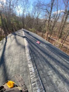 View of an asphalt shingle roof, with worn areas. Sunlight, trees in background.