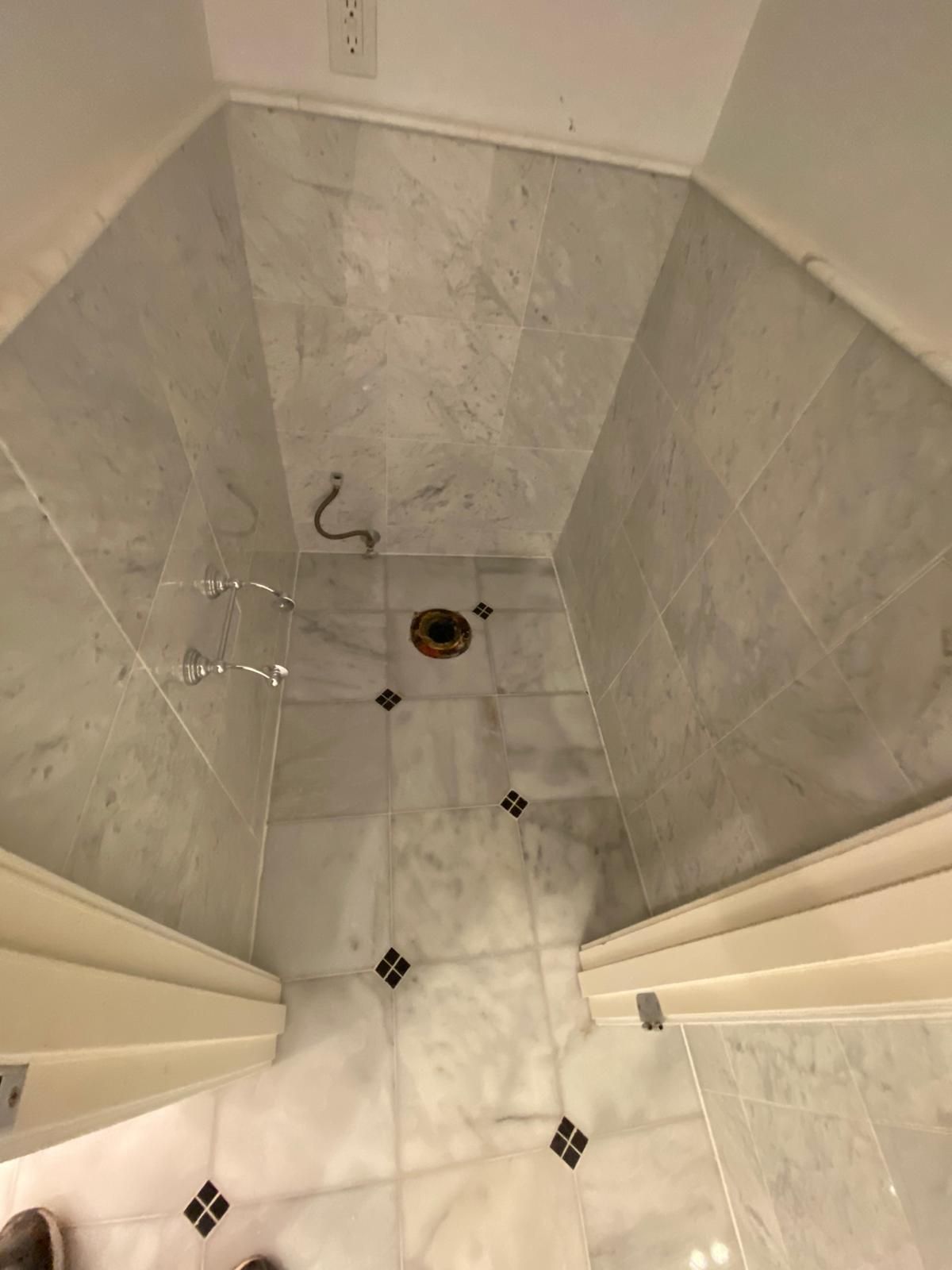 Marble-tiled bathroom floor with toilet flange, surrounded by walls, with decorative black accents.