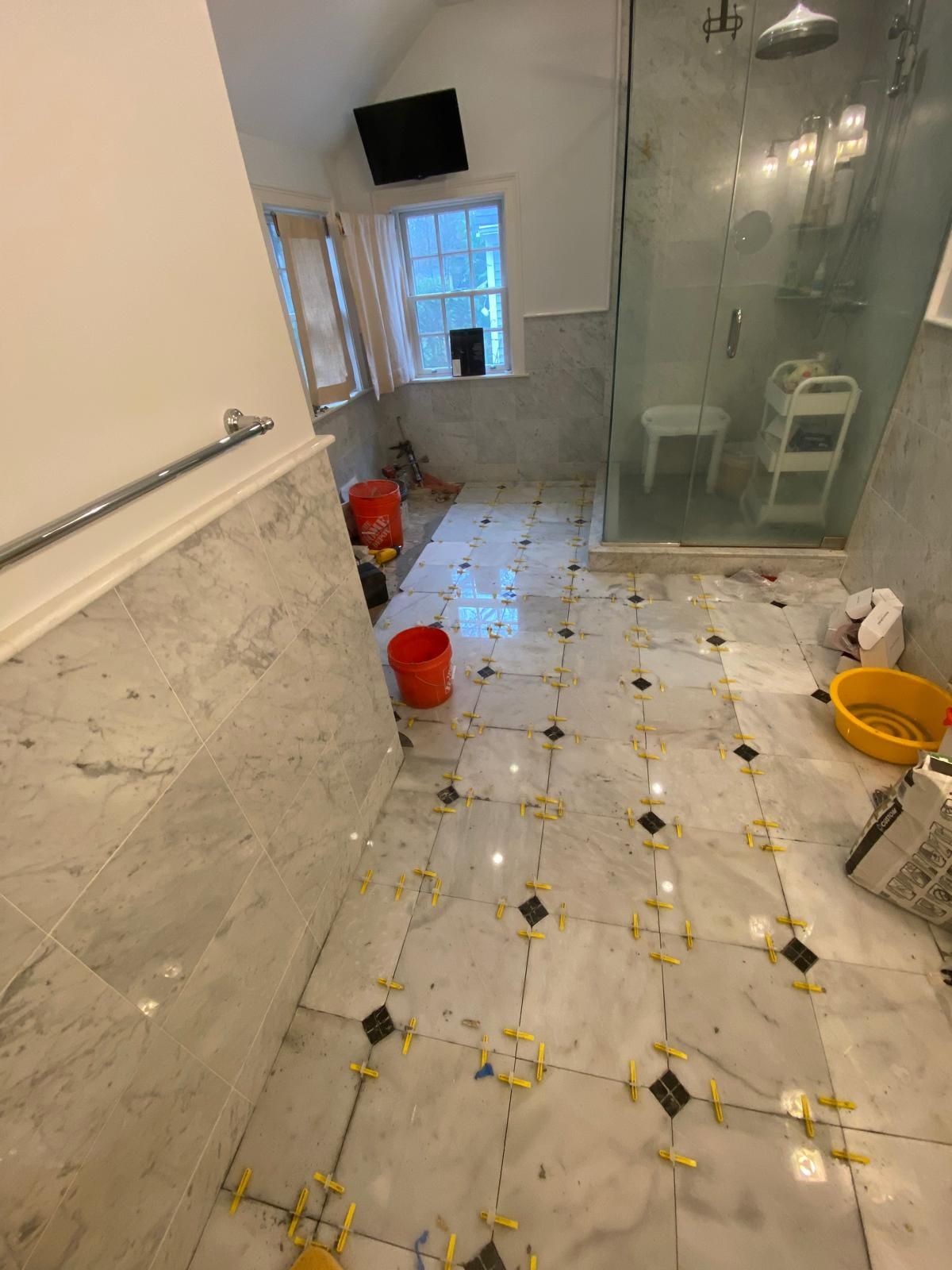 Bathroom under construction with marble tile floor and walls; orange buckets and tools present.