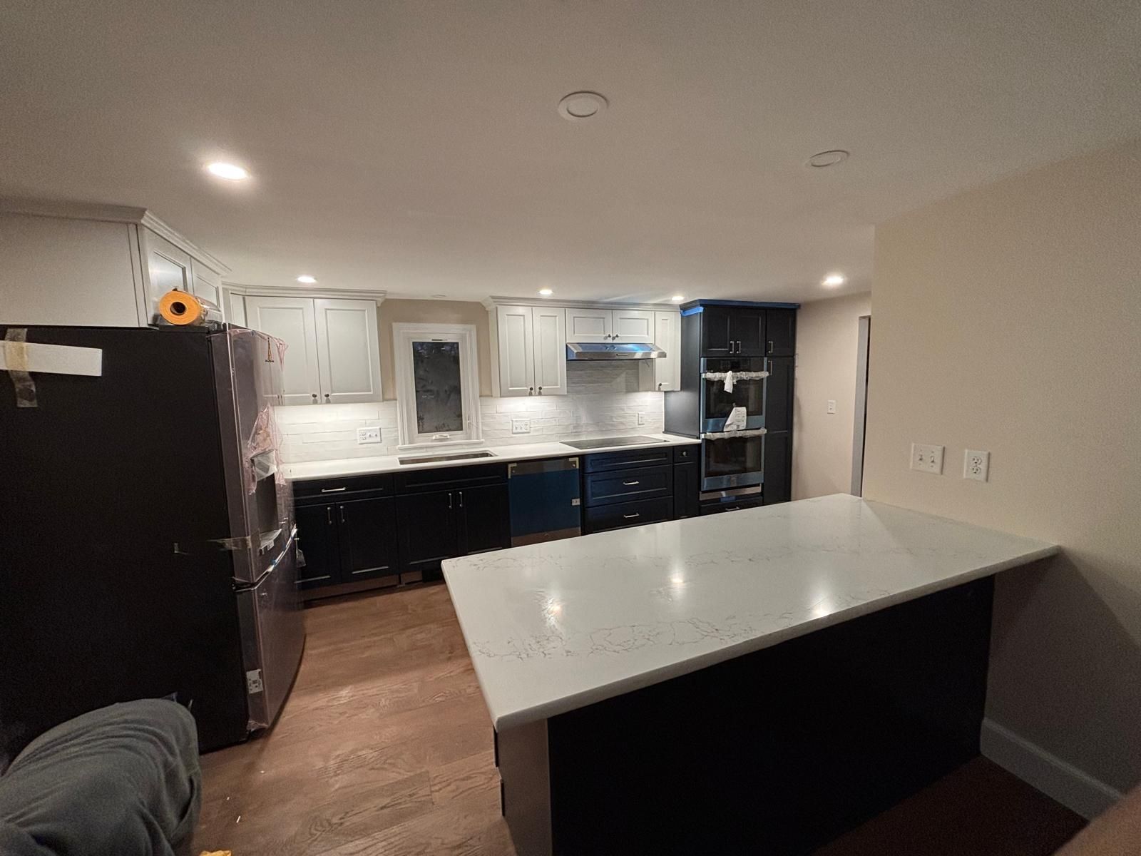 Modern kitchen with dark and light cabinets, a white countertop island, and a black refrigerator.