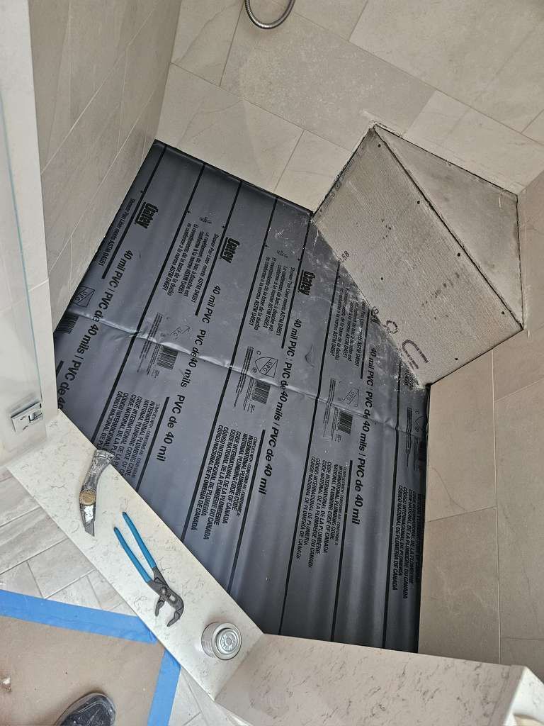Shower construction: Black waterproof membrane installed on a sloped shower floor, ready for tiling.