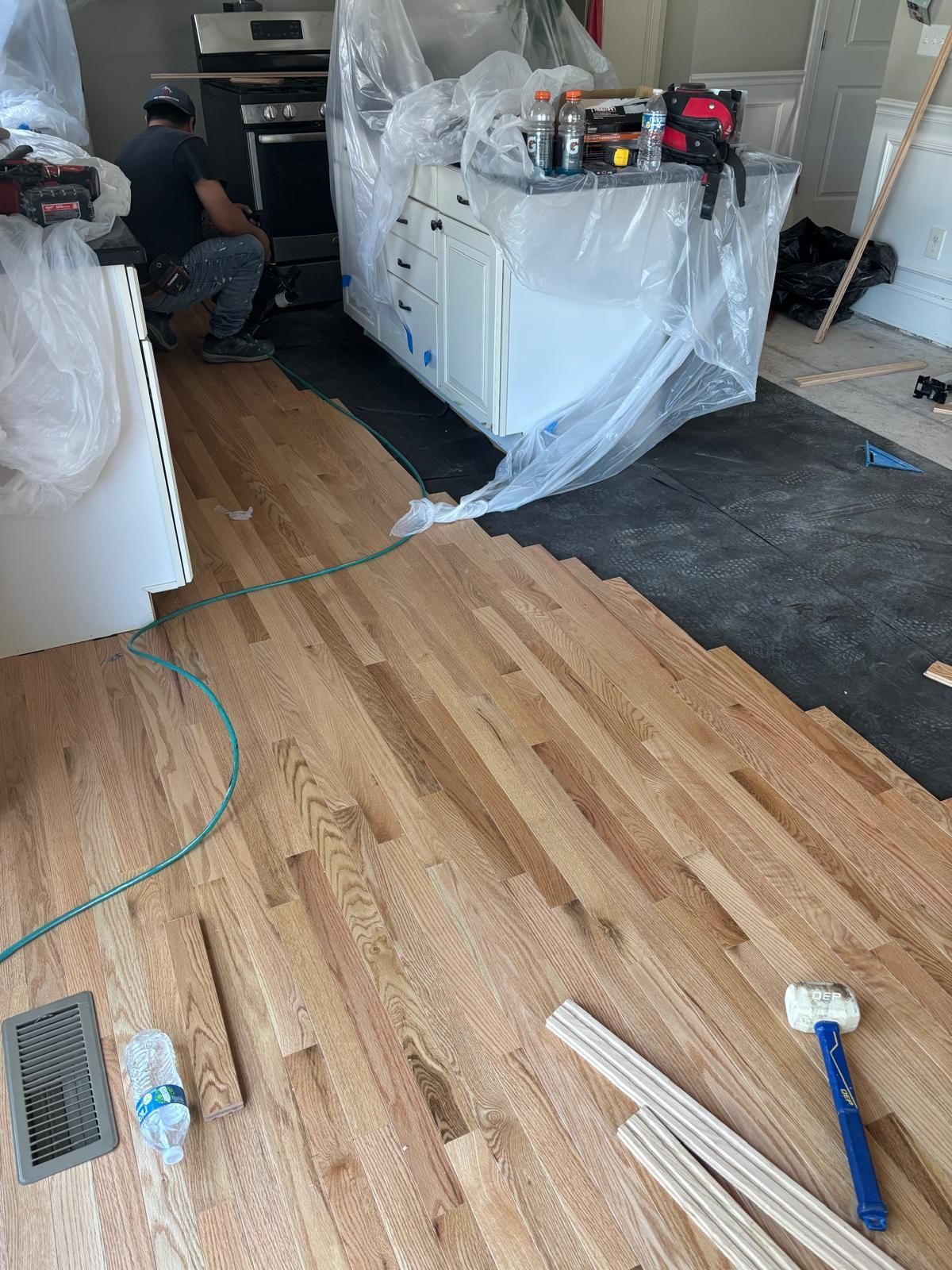 Hardwood floor installation in progress; worker near kitchen island.