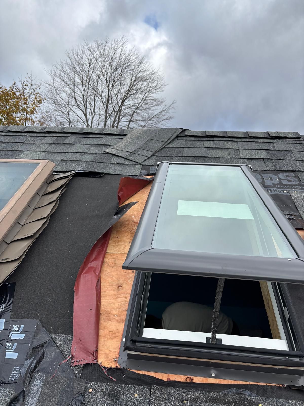 Roof with skylight under construction, exposed plywood and black roofing felt.