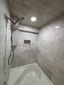 A tiled shower with a built-in shelf and overhead showerhead.