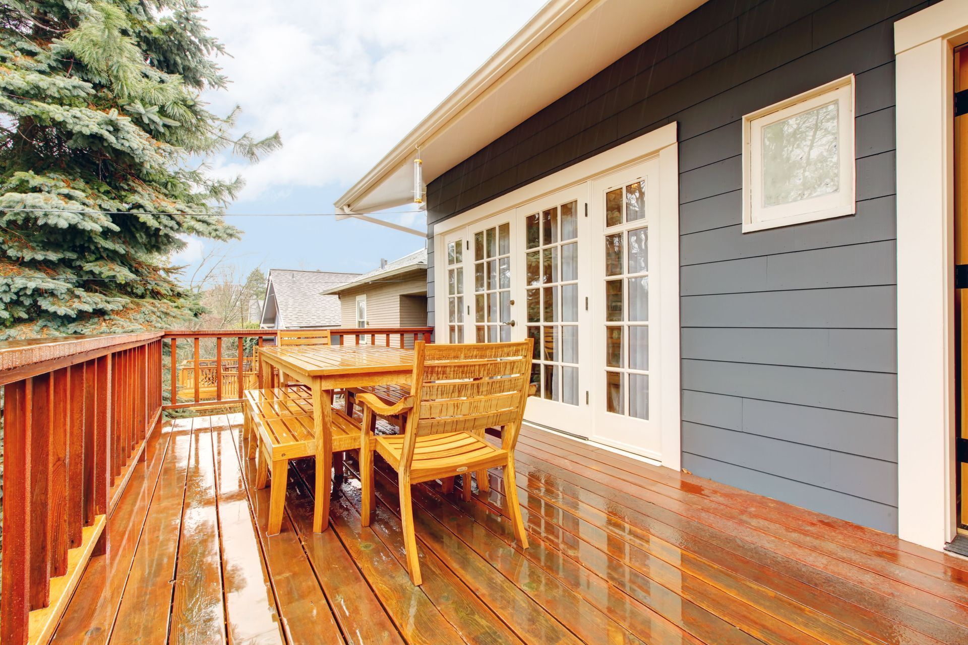 Wooden deck with table and chairs, adjacent to a dark gray house with French doors.