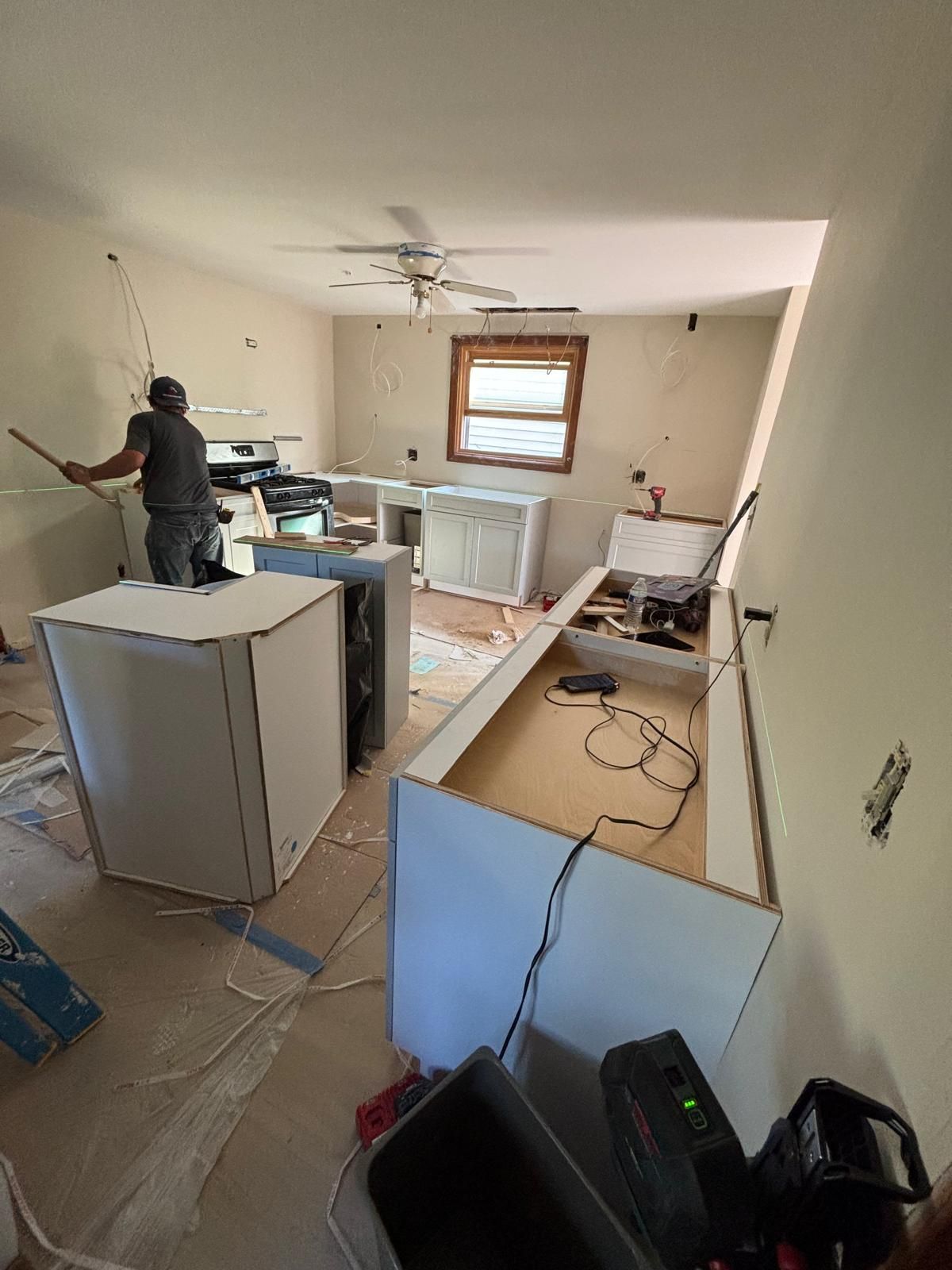 Kitchen renovation: cabinets partially installed, worker standing near a counter, tools and wiring visible.