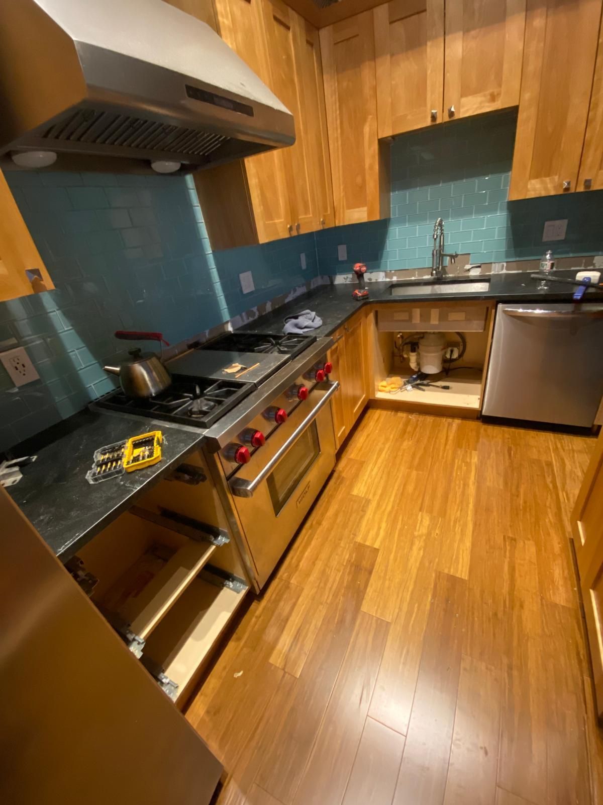 Kitchen renovation with wooden cabinets, blue tile backsplash, stainless steel appliances, and partially installed countertop.