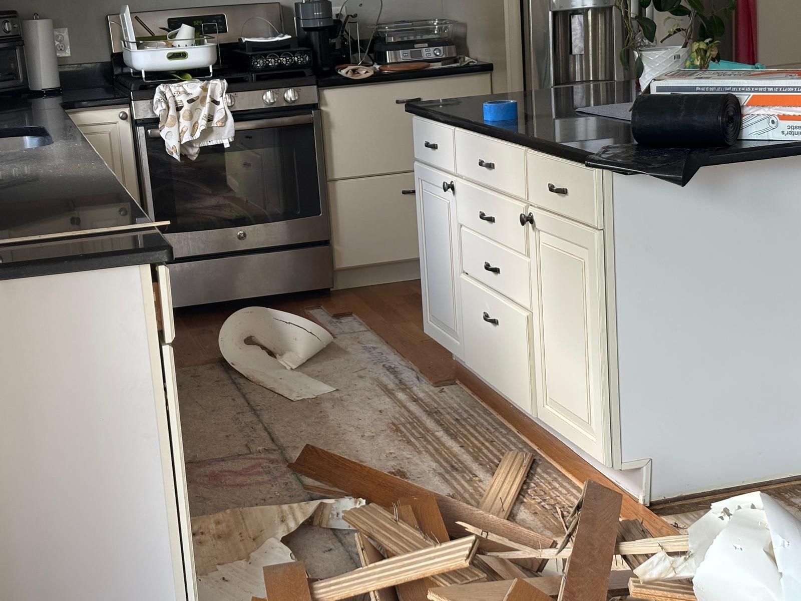 Kitchen with black countertops, white cabinets, and damaged flooring; demolition debris.