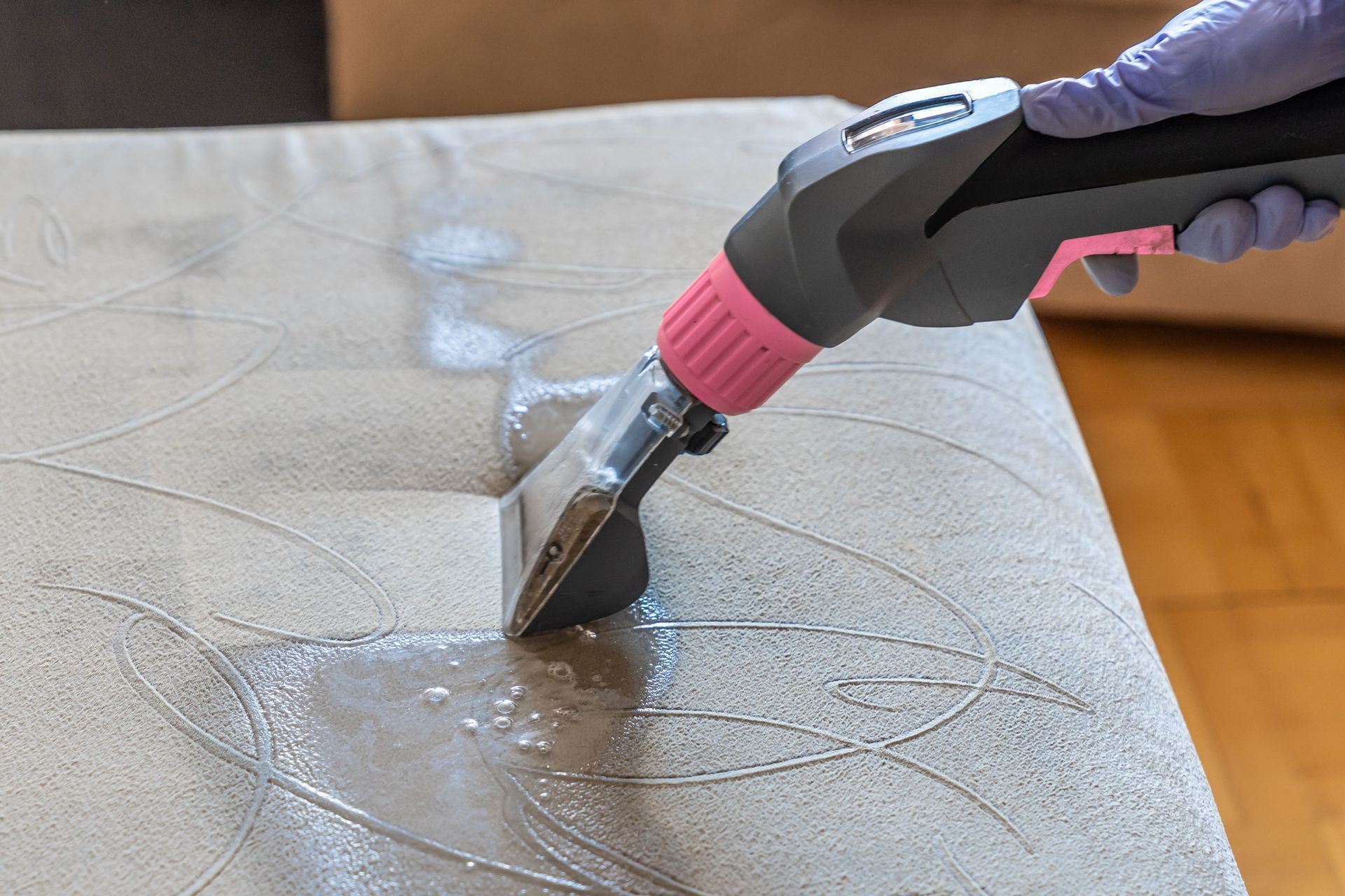 Person using a steam cleaner on a light-colored sofa, removing a stain.