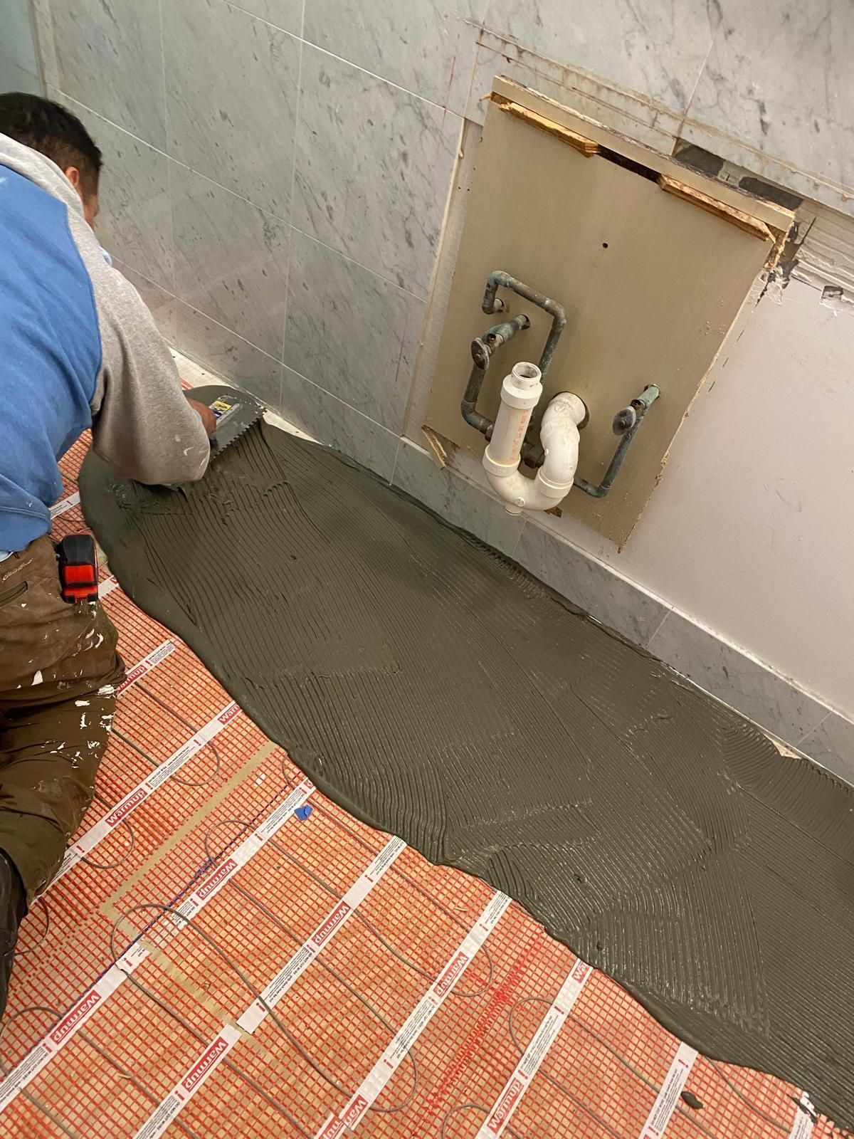 Person applying mortar to floor heating mat in bathroom.
