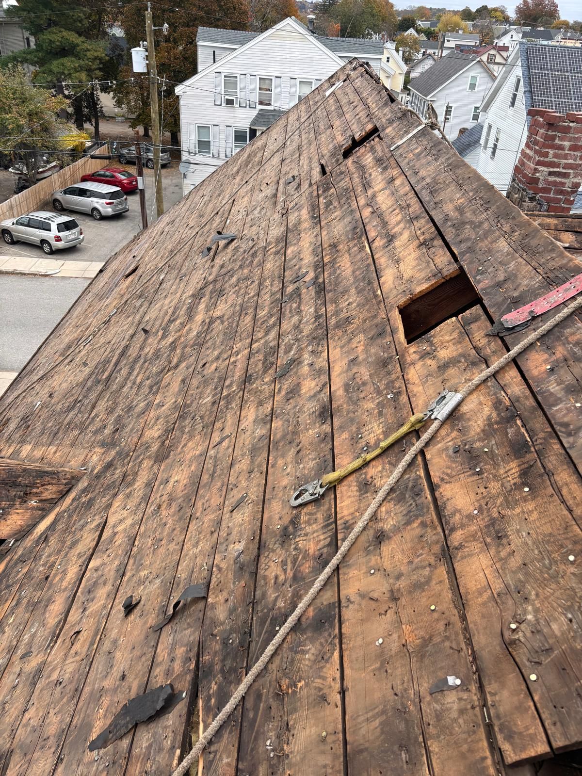 View of a weathered wooden roof with missing sections, a safety rope, and surrounding buildings.