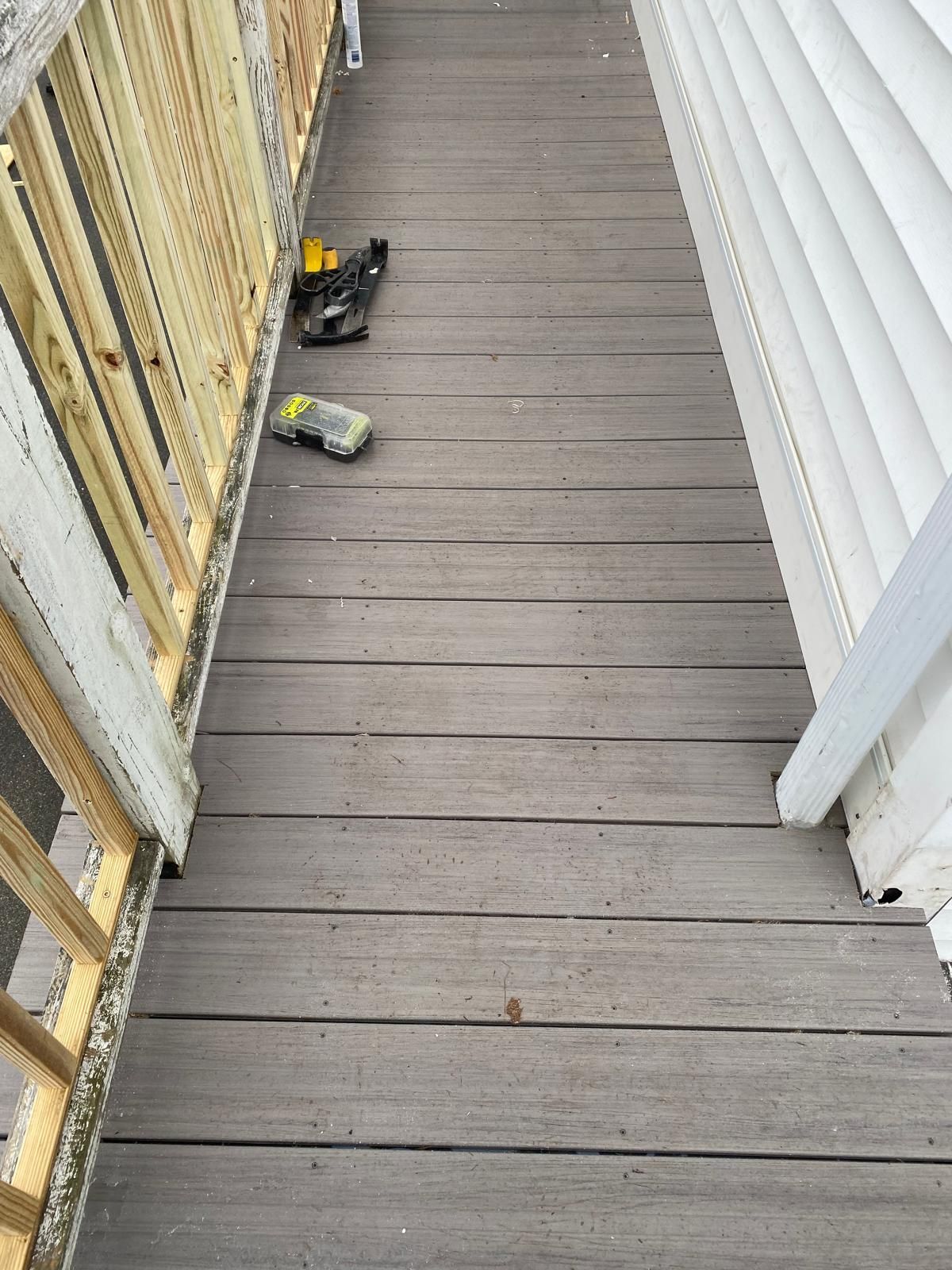 Wooden deck with tools, next to a railing and siding.