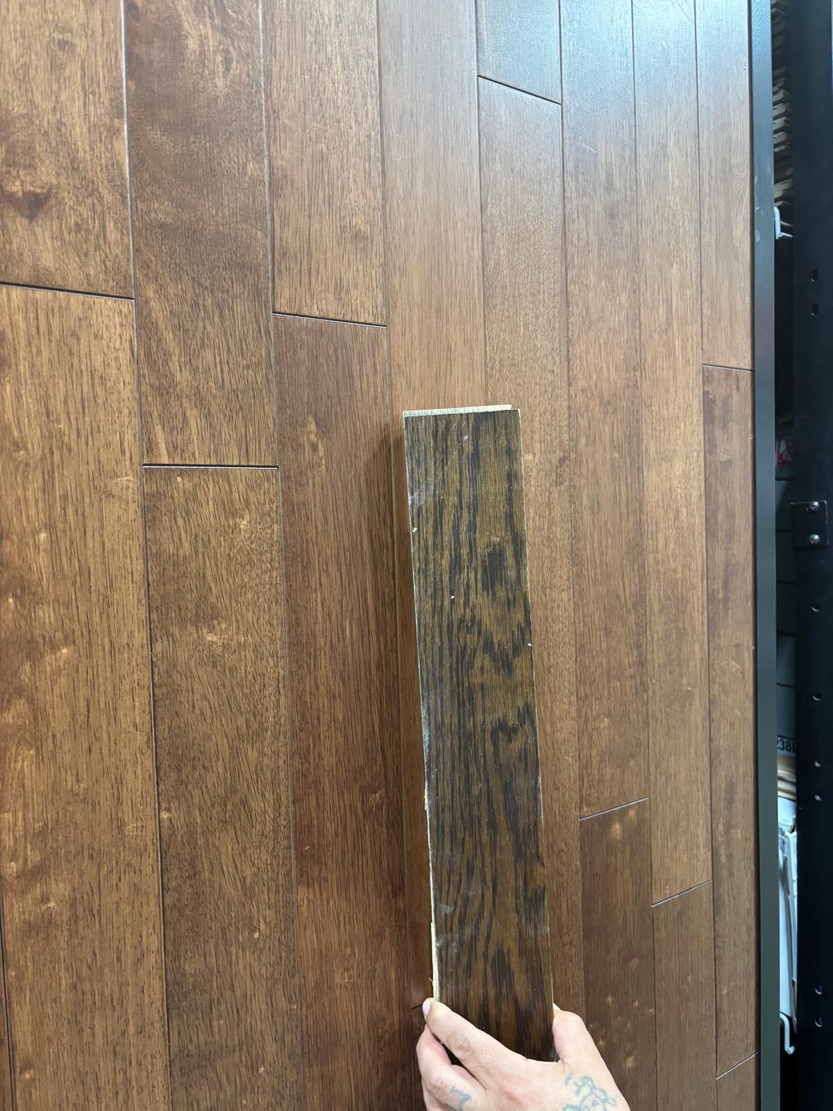 Hand holding a dark wood floor sample against installed dark wood flooring.
