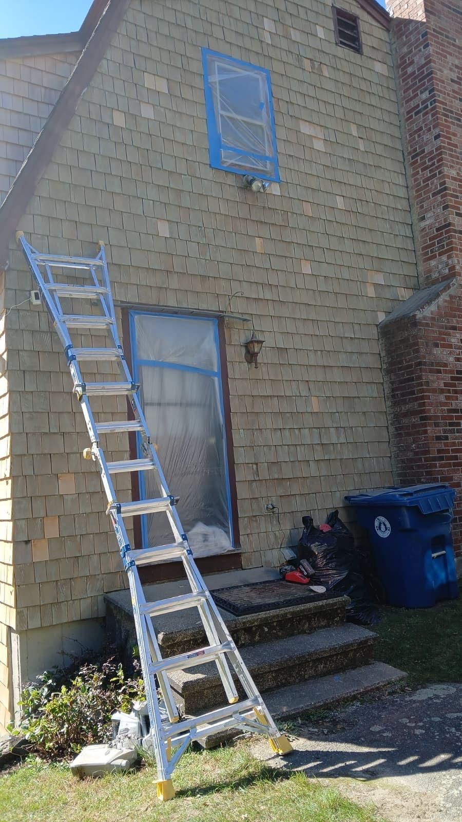 Ladder leaning against house, window and door taped for painting.