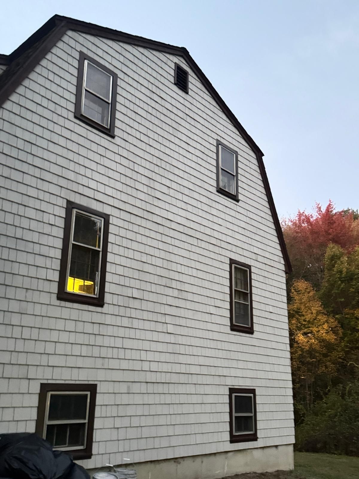 White shingled house exterior with brown trim, six windows, and a dark roof.