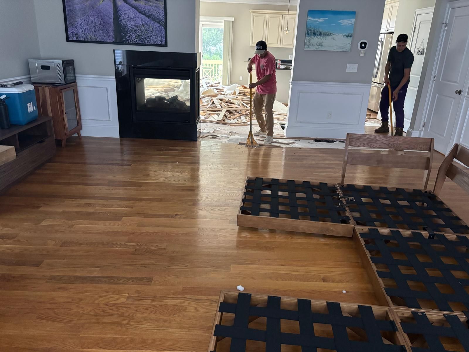 Men removing debris during a home renovation; wooden floor, fireplace, and furniture in foreground.