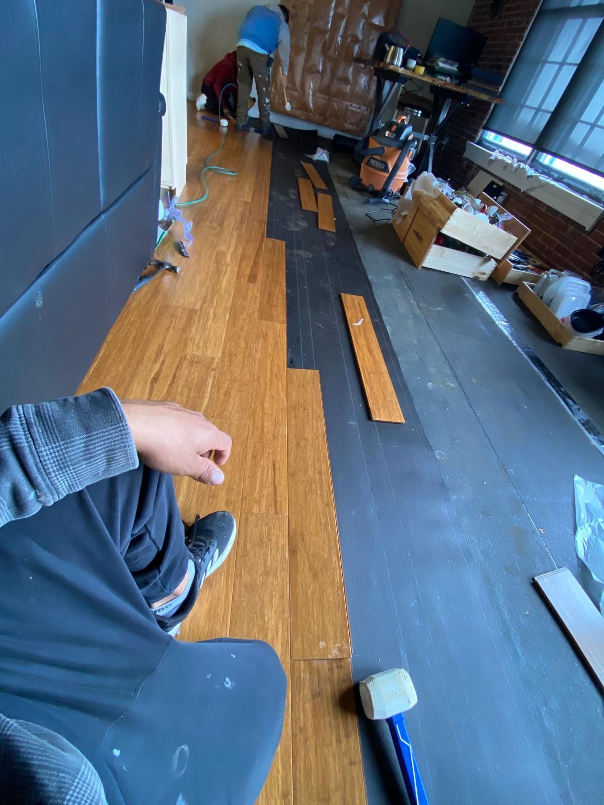 Bamboo flooring being installed in a room; workers, tools, and materials visible.
