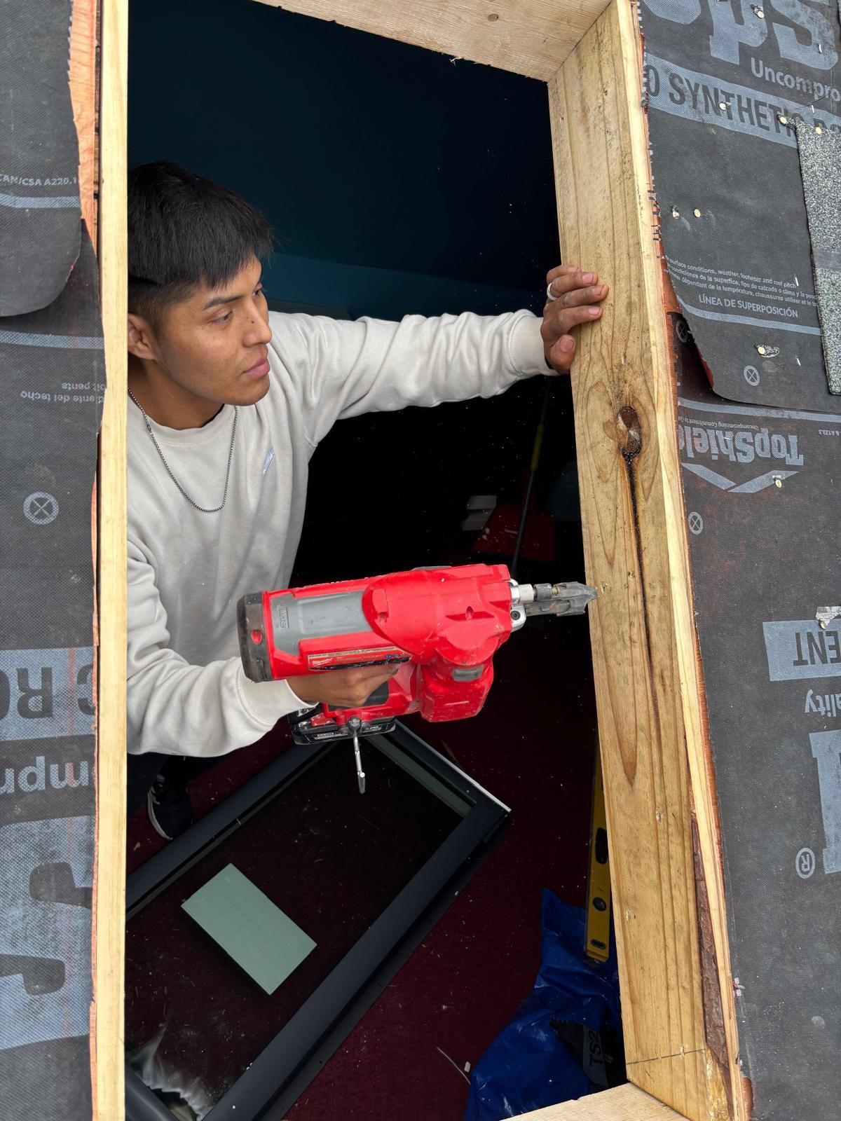 Man using a red nail gun to install wood in a window frame, outdoors.