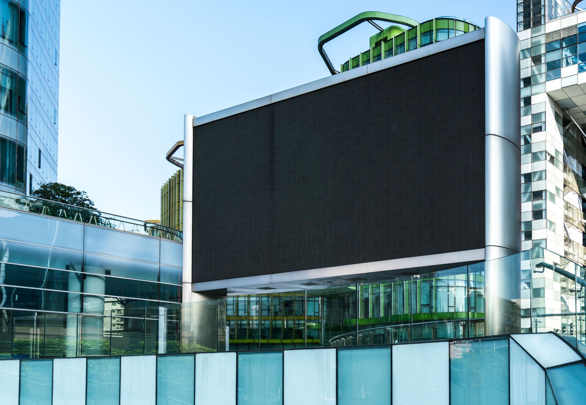Large, blank digital billboard, silver frame, surrounded by modern glass and steel buildings.