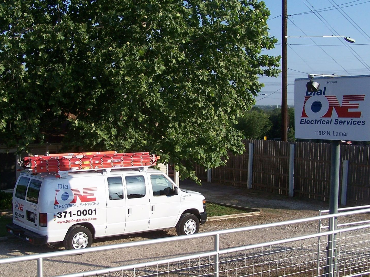 White van with ladder on roof, parked next to a small building and sign for