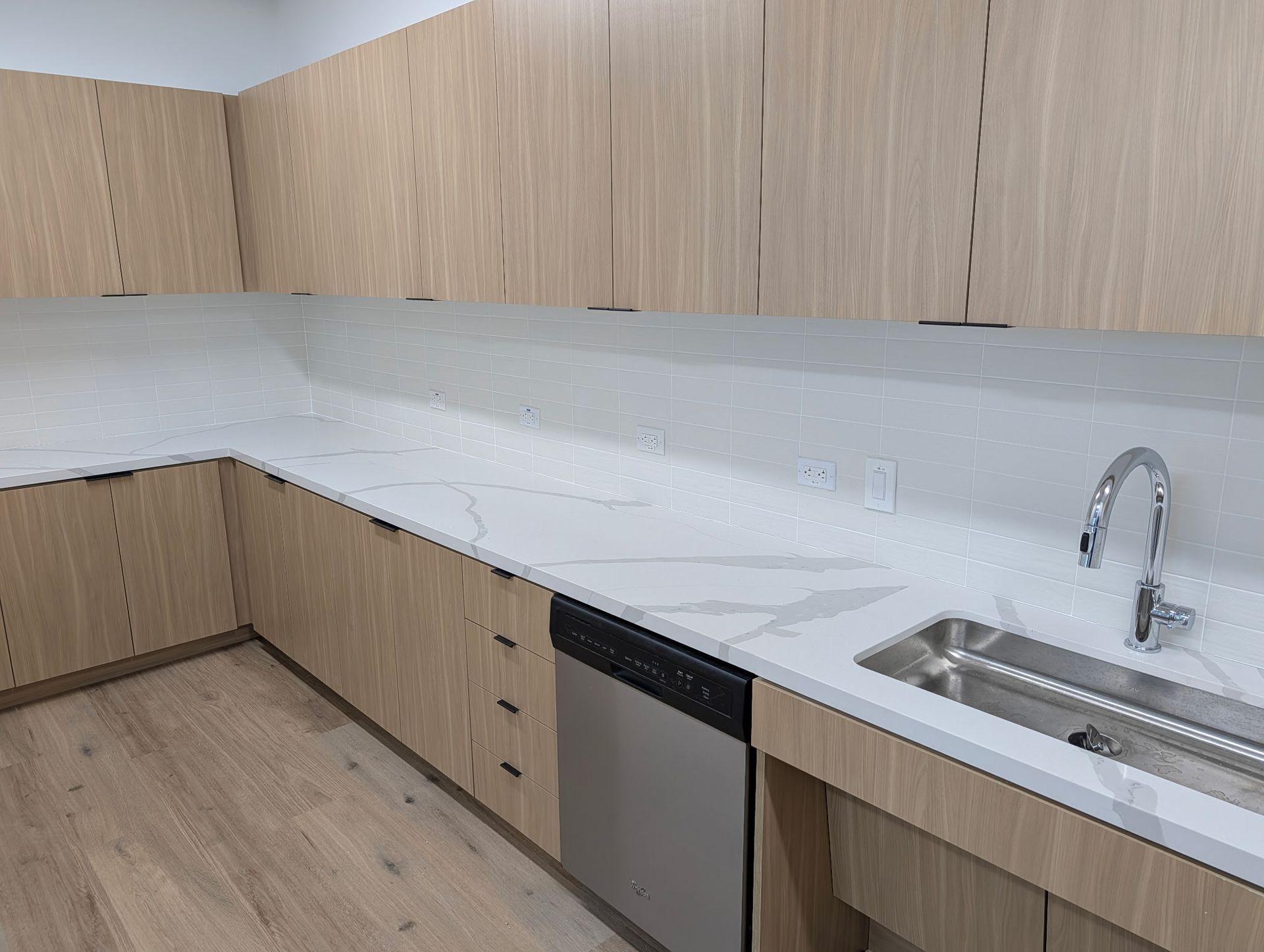 Kitchen with light wood cabinets, white countertops, stainless steel sink and dishwasher.