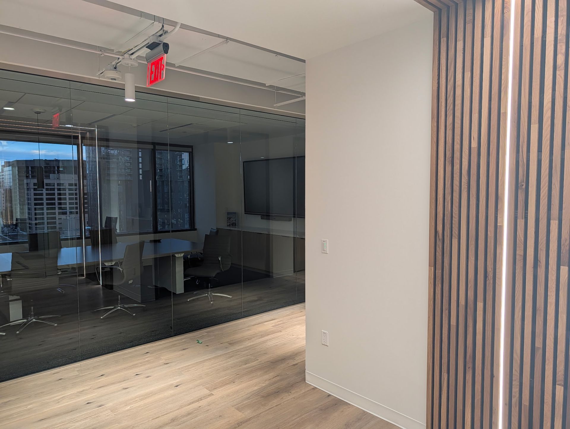 Office interior with glass walls, wooden panel, and hardwood floor.