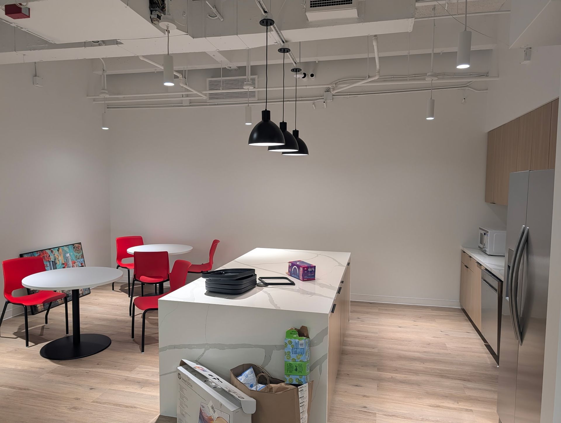 Office breakroom with island, tables, red chairs, and stainless steel appliances.