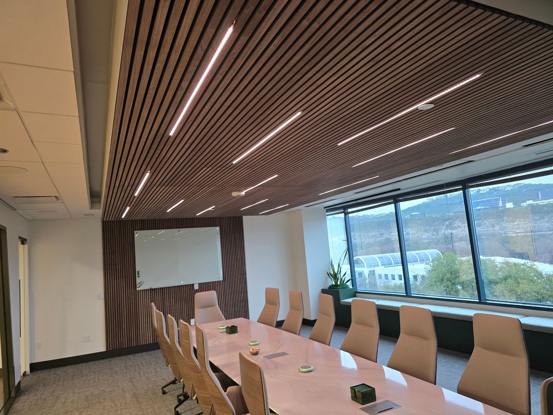 Conference room with a wooden slatted ceiling, long table, chairs, and large window with a view.