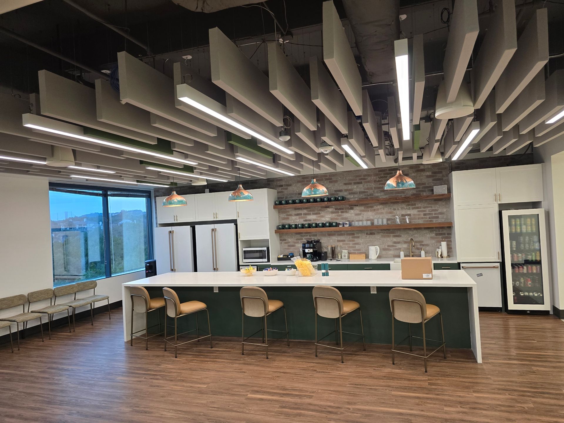Modern office kitchen with long island, chairs, appliances, and interesting ceiling design.