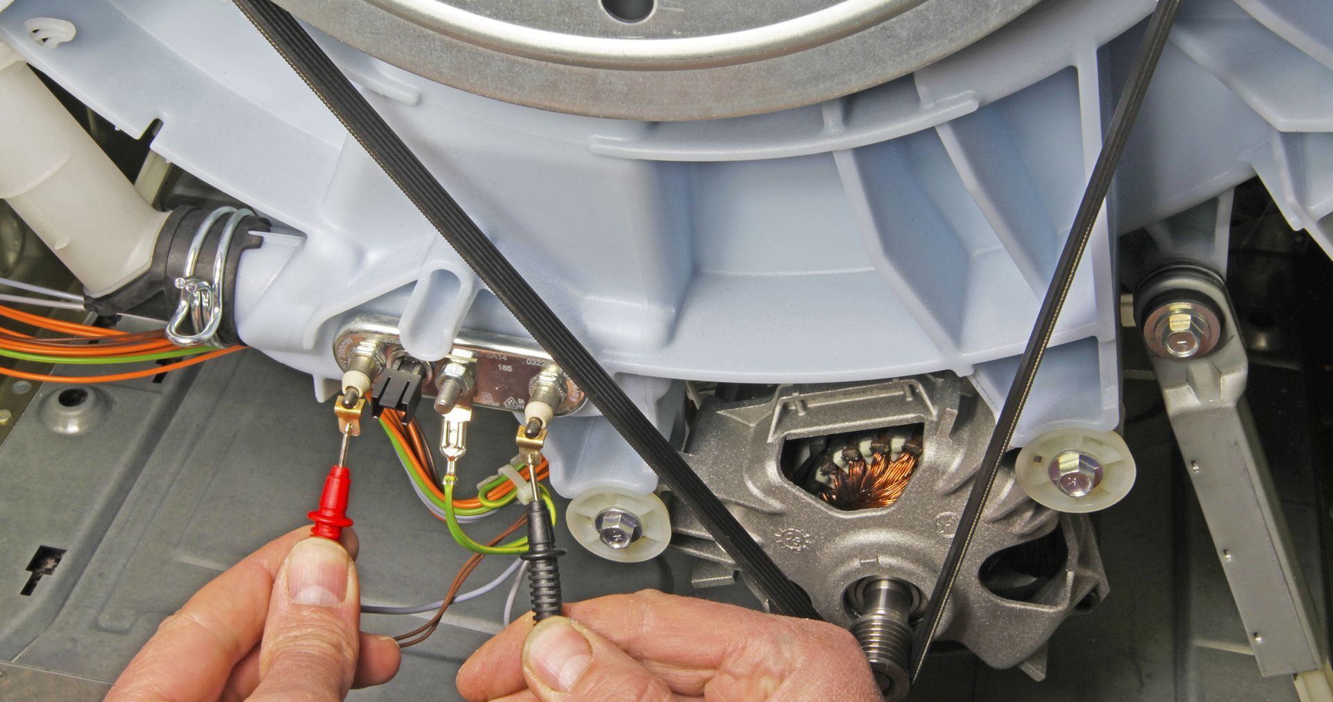 Hands testing electrical connections on a washing machine motor.