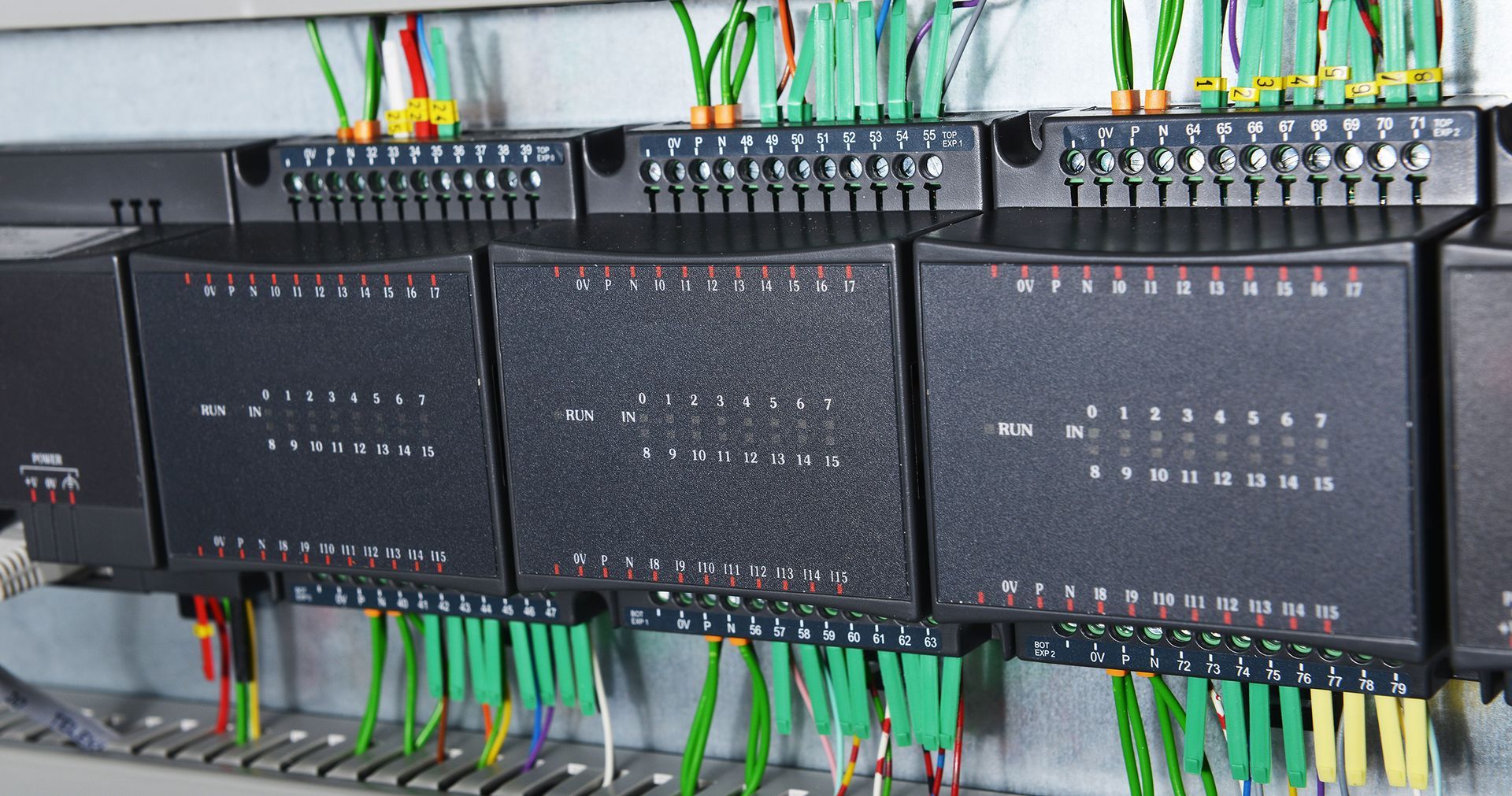 Close-up of industrial electrical panel with black modules, green wires, and numbered terminals.