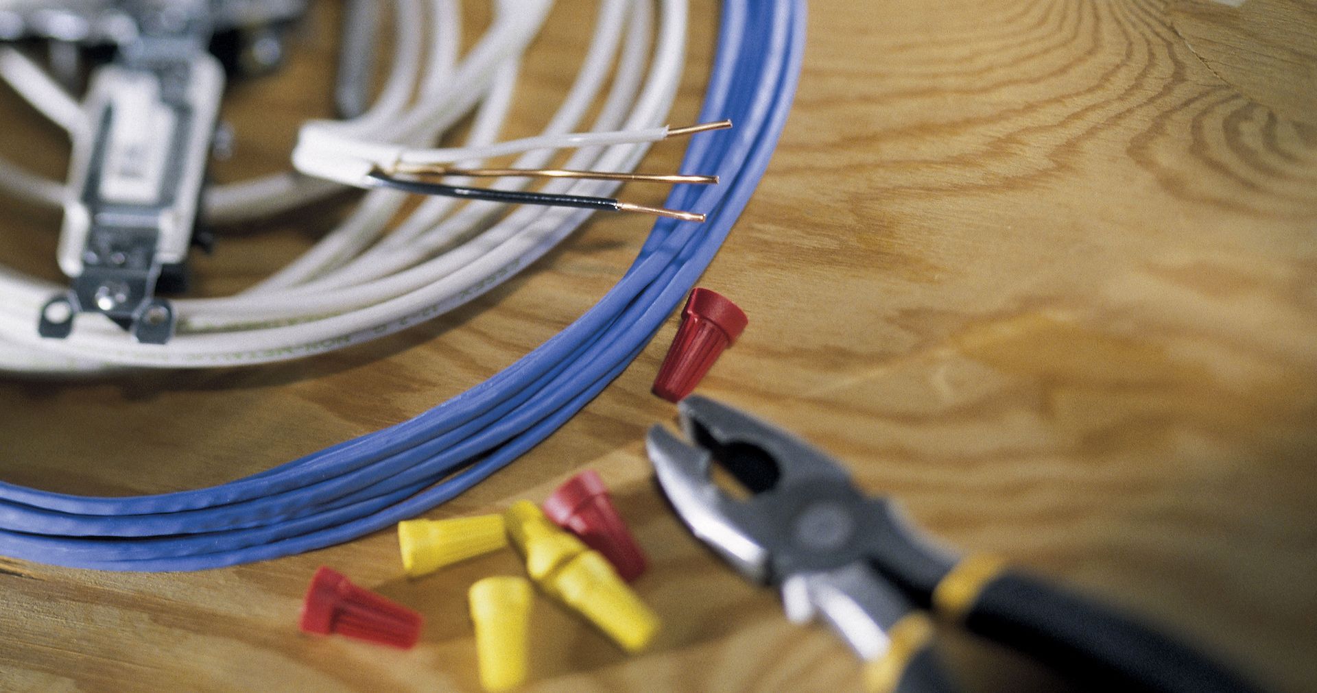Electrical wiring with wire connectors and pliers on wood.