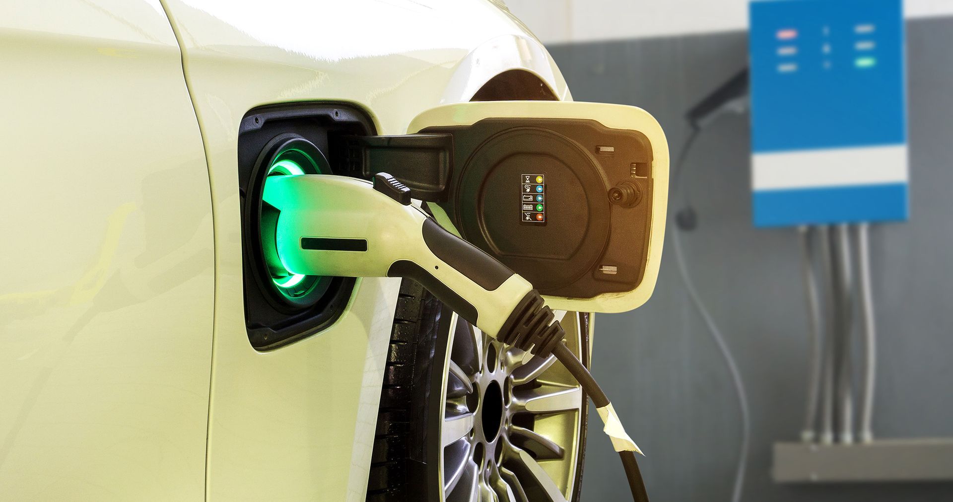 White electric car charging with a green glowing plug. A blue charger is in the background.