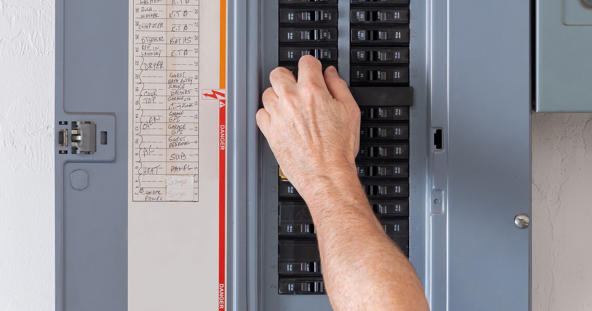 Hand flipping a circuit breaker switch in a grey electrical panel.