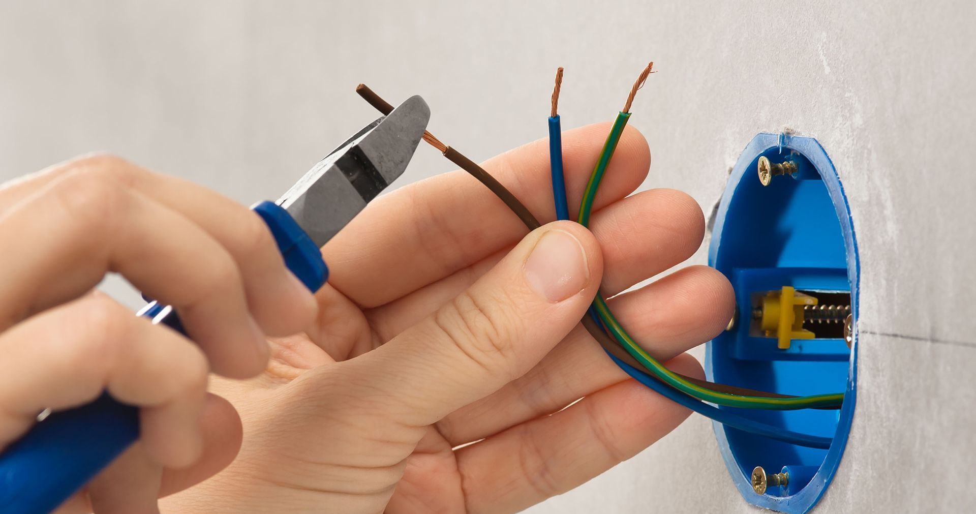 Person using pliers to strip electrical wires near a blue electrical box.