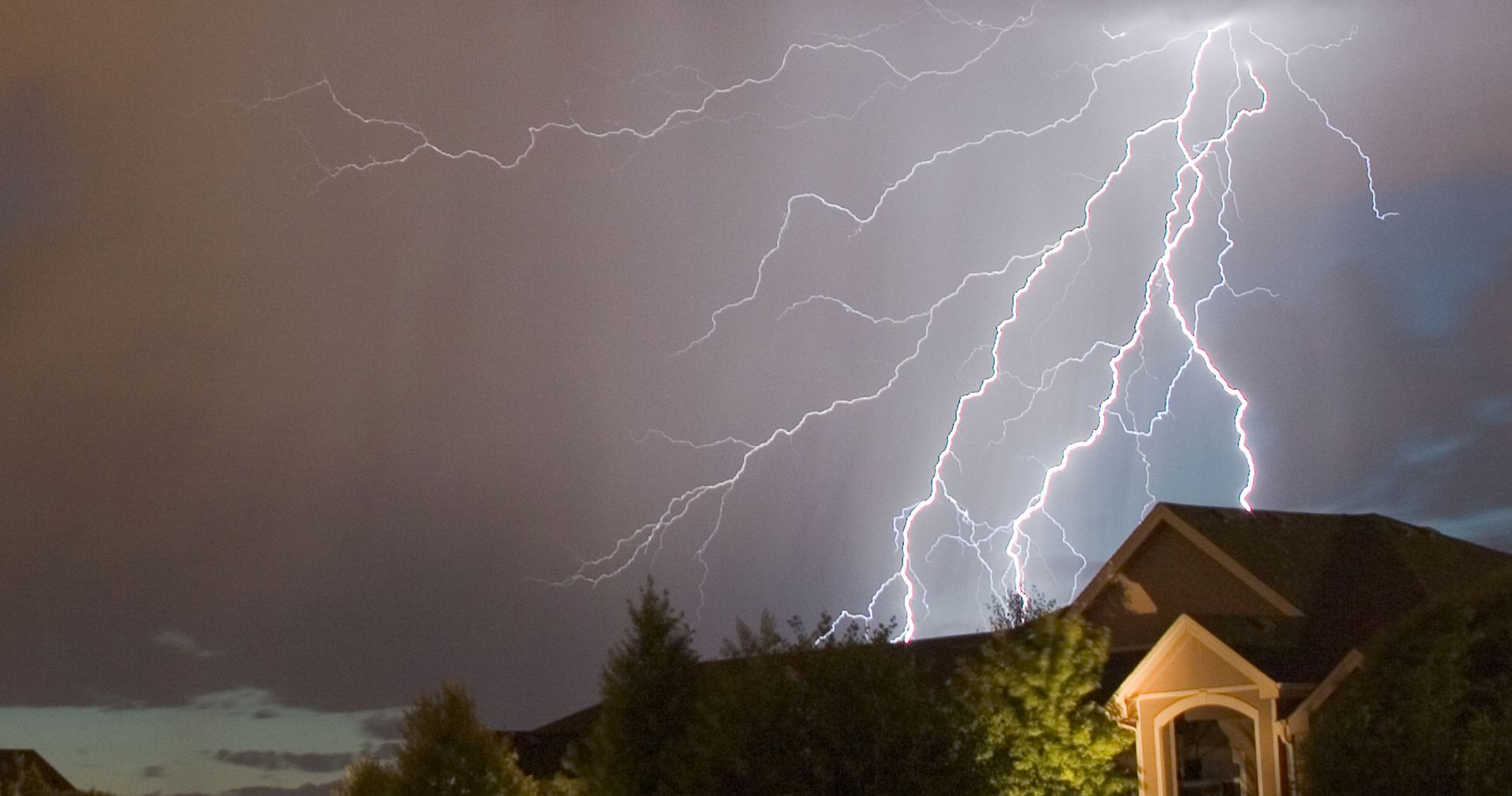 Lightning strikes over a house at night, illuminating the dark sky.