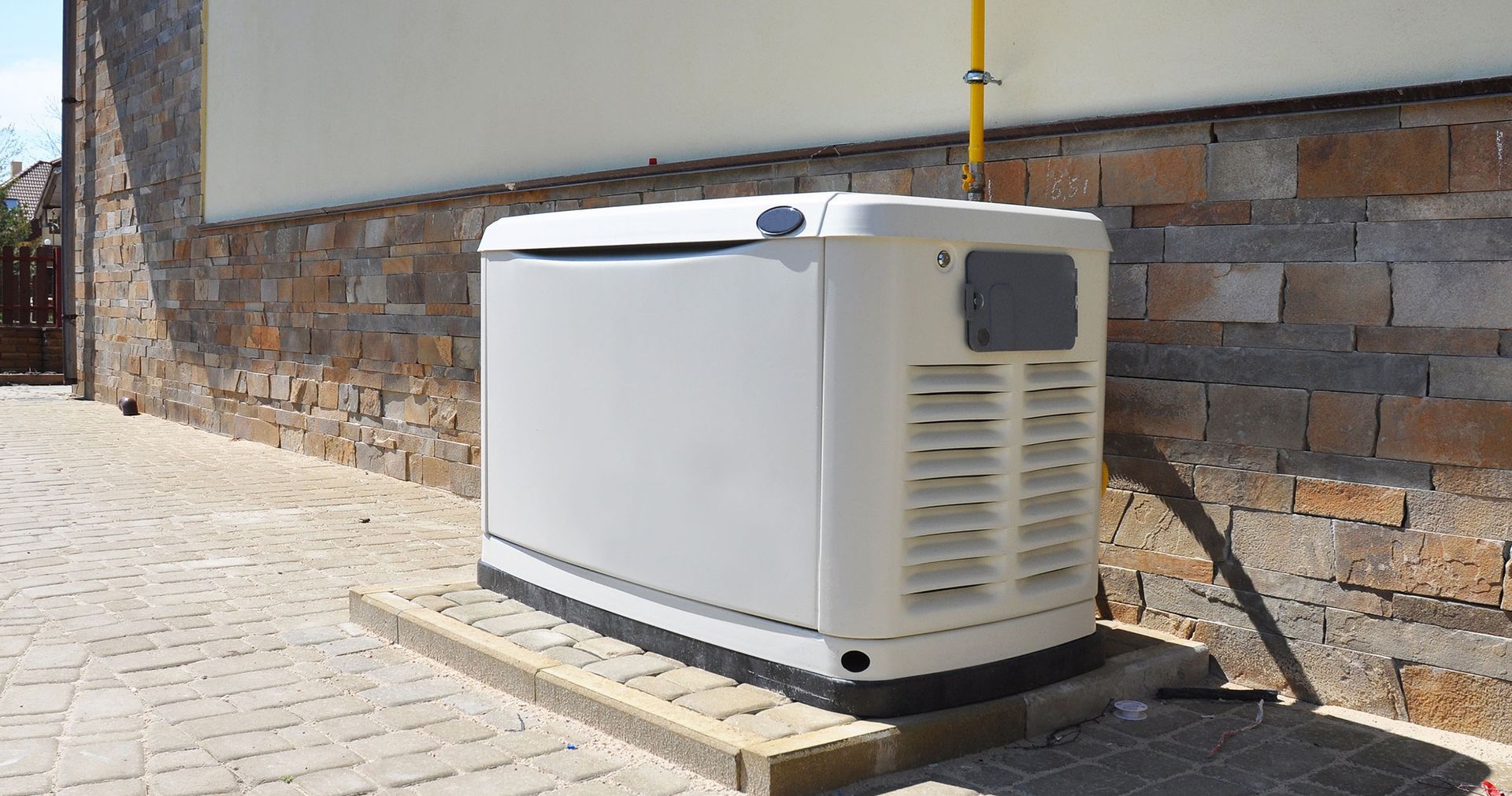 White generator on a concrete pad next to a brick wall. A yellow gas line is visible.