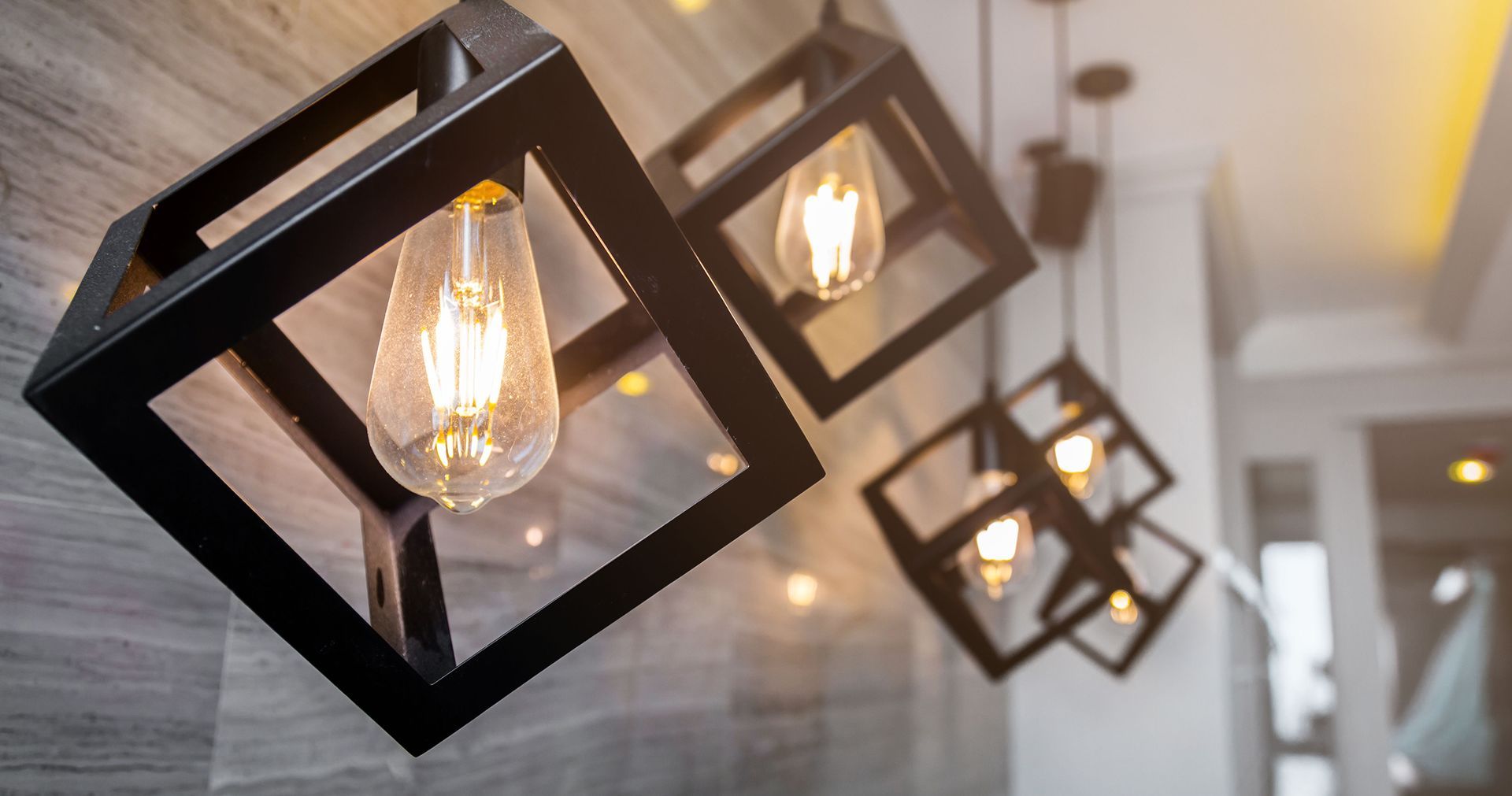Black geometric cube pendant lights with Edison bulbs on a textured wall.