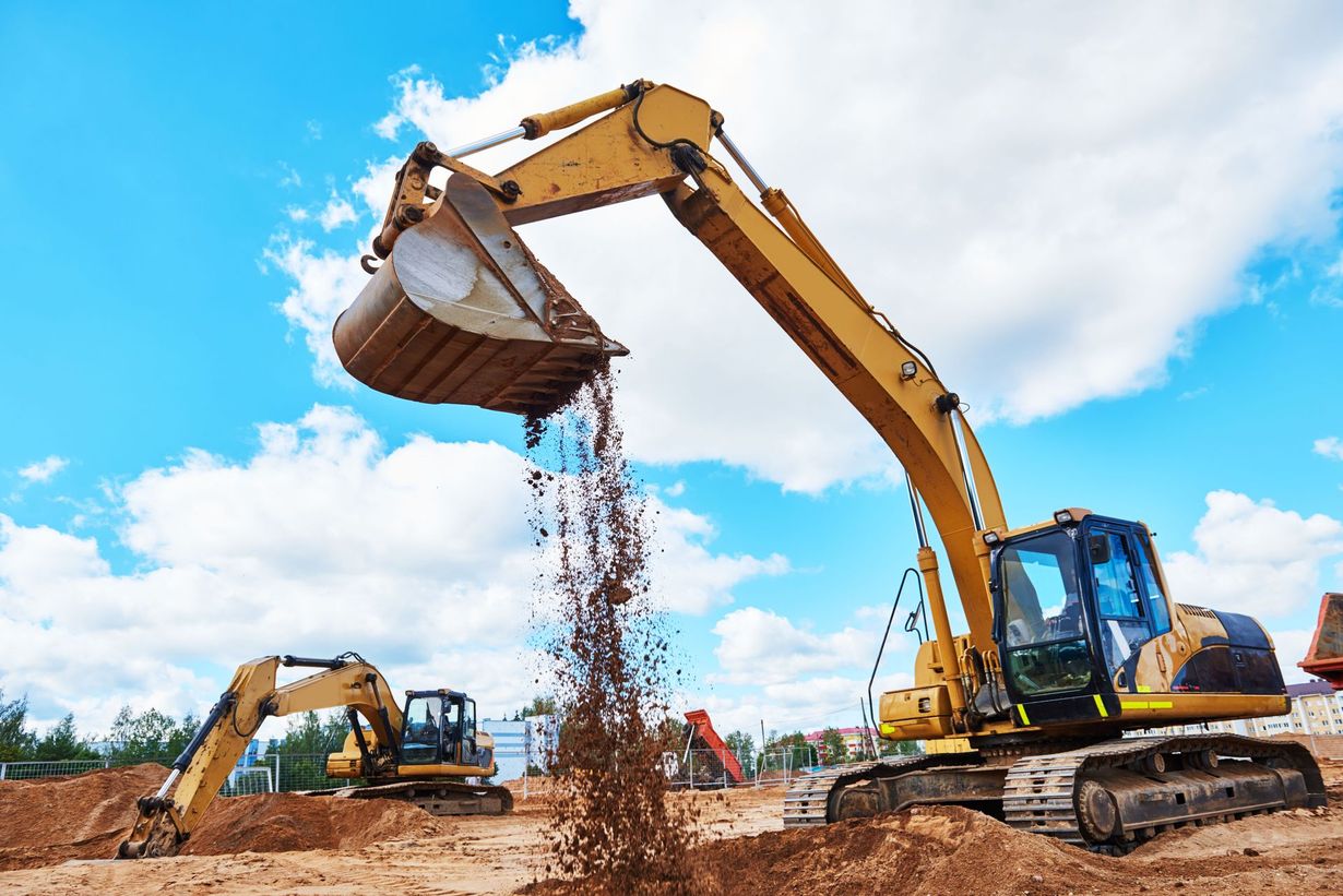 Yellow excavator pouring dirt at a construction site under a blue sky, with another excavator in the background