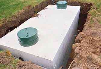 Rectangular concrete septic tank with two green access lids in a dug-out yard