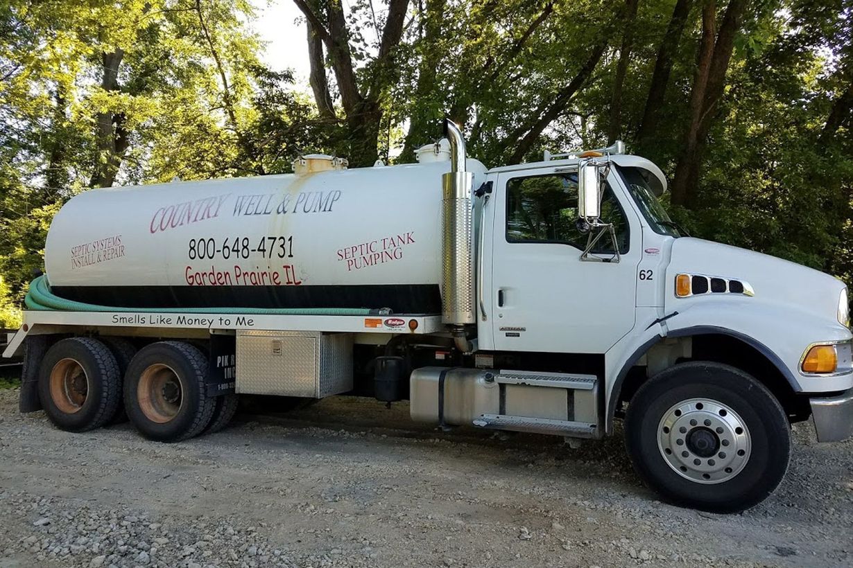 White tanker truck parked on gravel with trees in the background