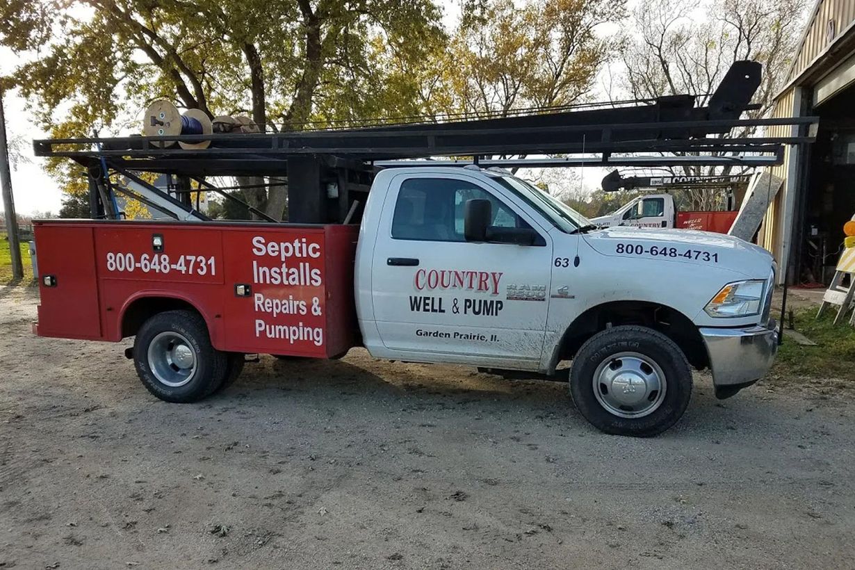 White and red plumber’s service van with ladder rack parked on a dirt road by trees