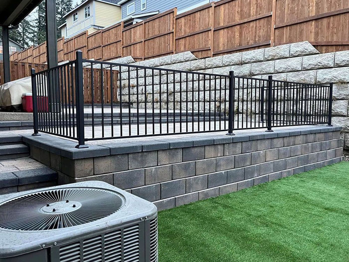 A backyard with a fence, stairs, a brick wall, and an air conditioner
