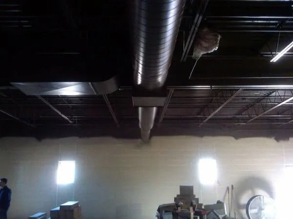 Warehouse ceiling with ventilation ducts, exposed beams, and a glimpse of a person and windows.