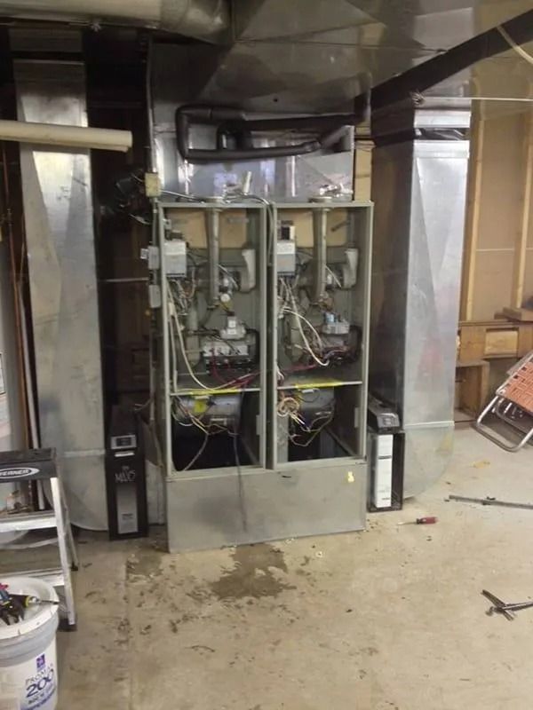 Two rectangular furnaces with exposed interiors, connected to ducts, in a basement.