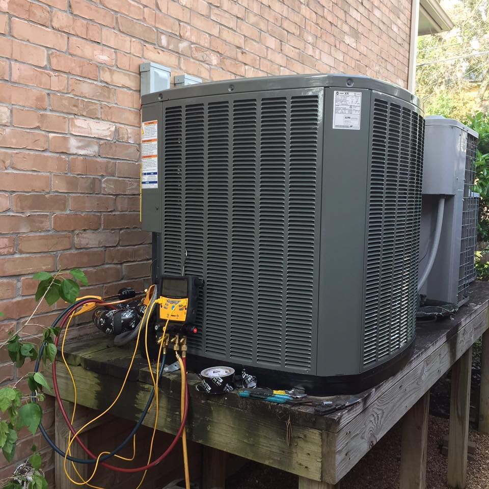 An air conditioning unit being serviced outdoors, with gauges and hoses connected.